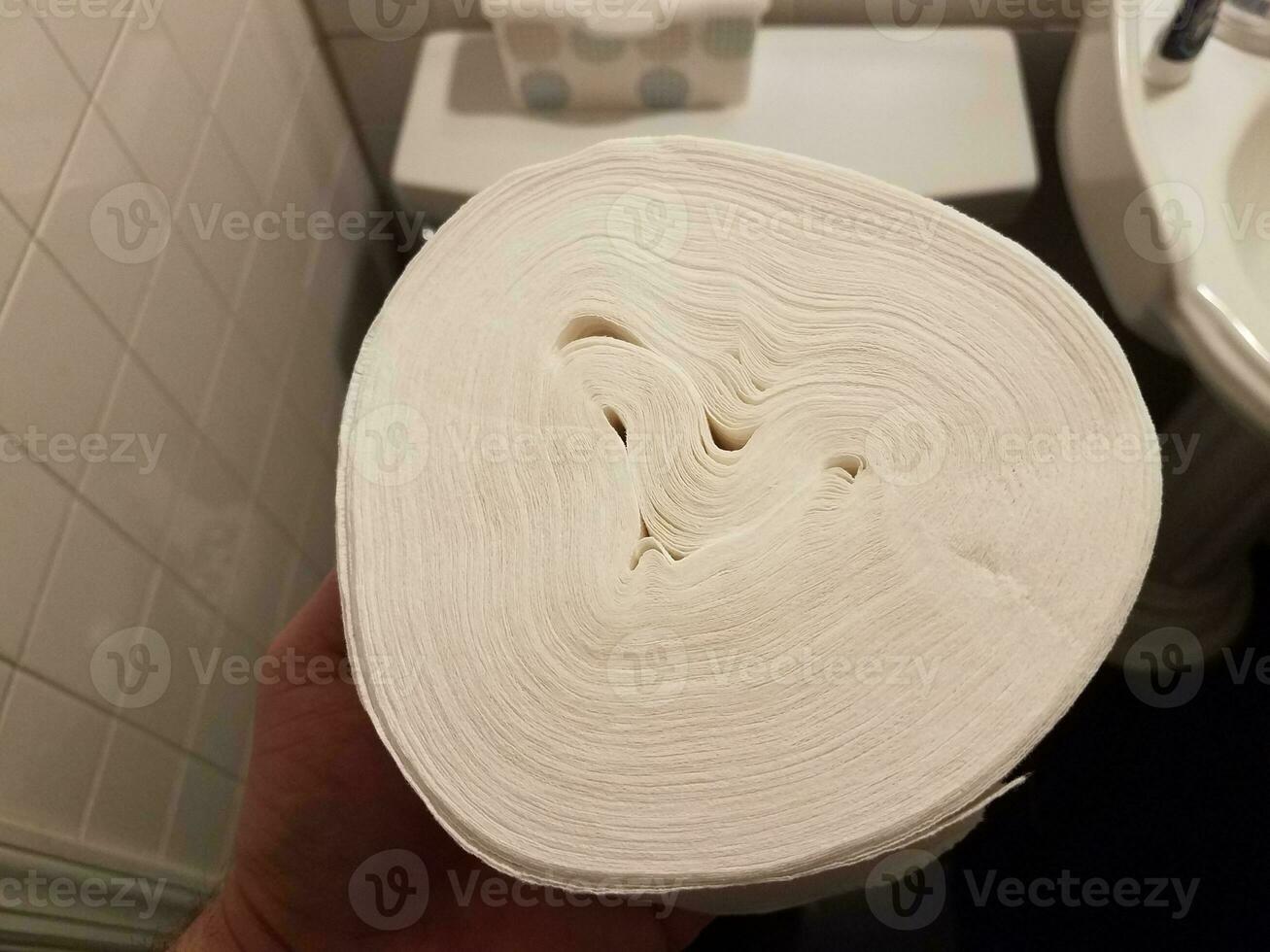 hand holding toilet paper roll without center over toilet photo