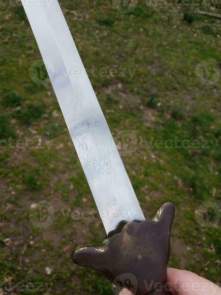 hand holding metal Chinese sword with copper handle photo