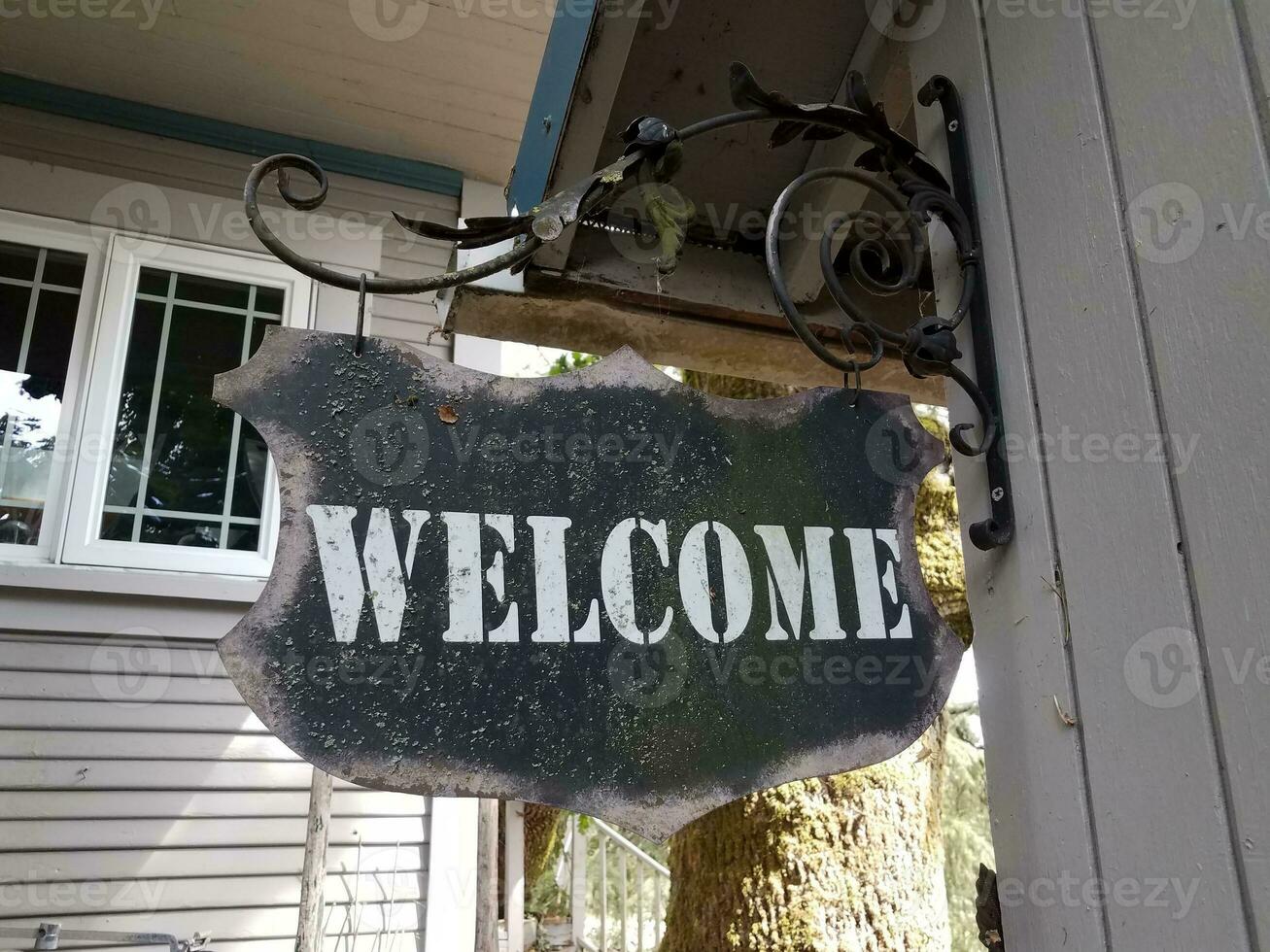 weathered black metal welcome sign hanging on wall photo