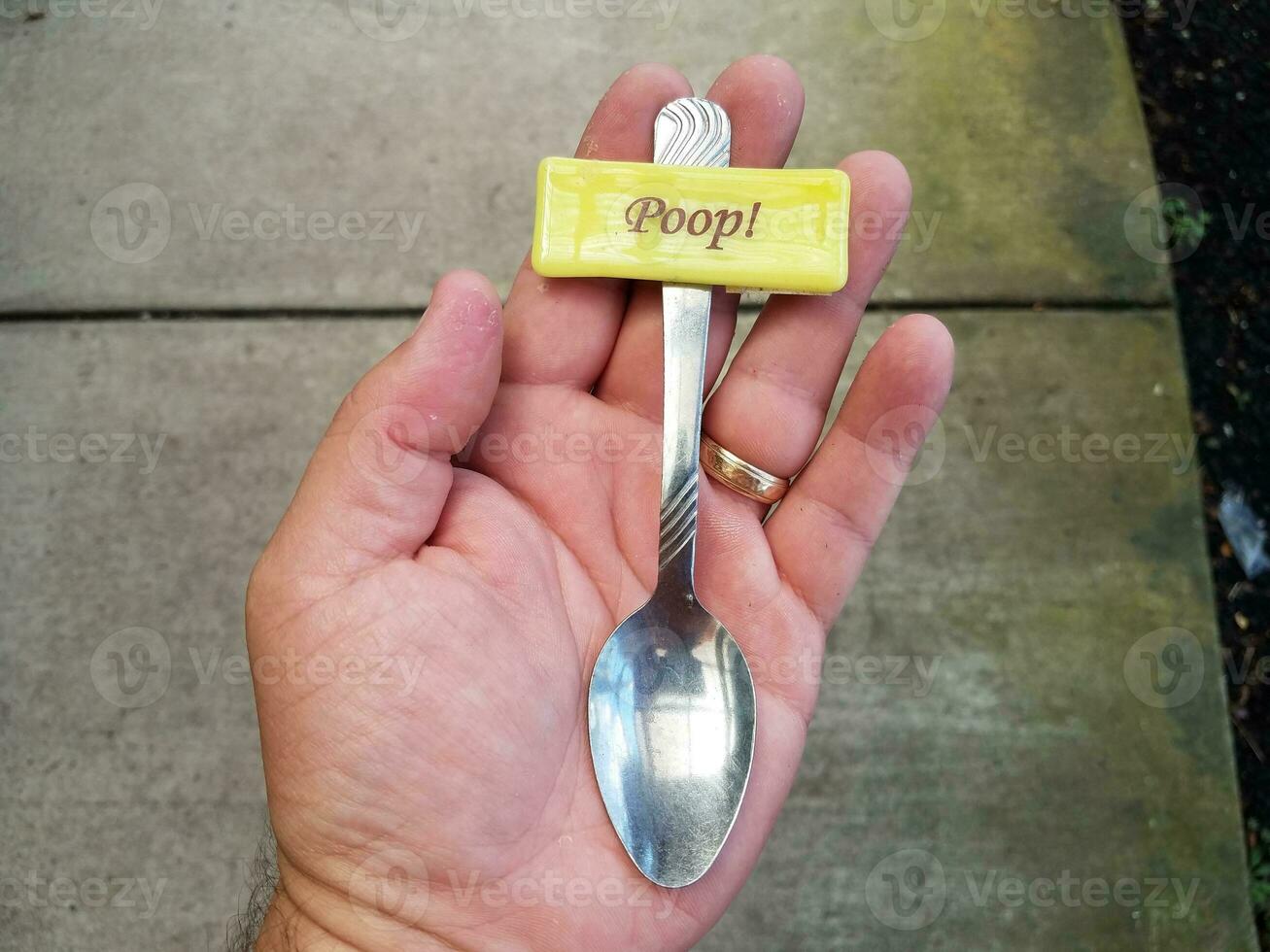 hand holding small spoon with poop sign over cement photo