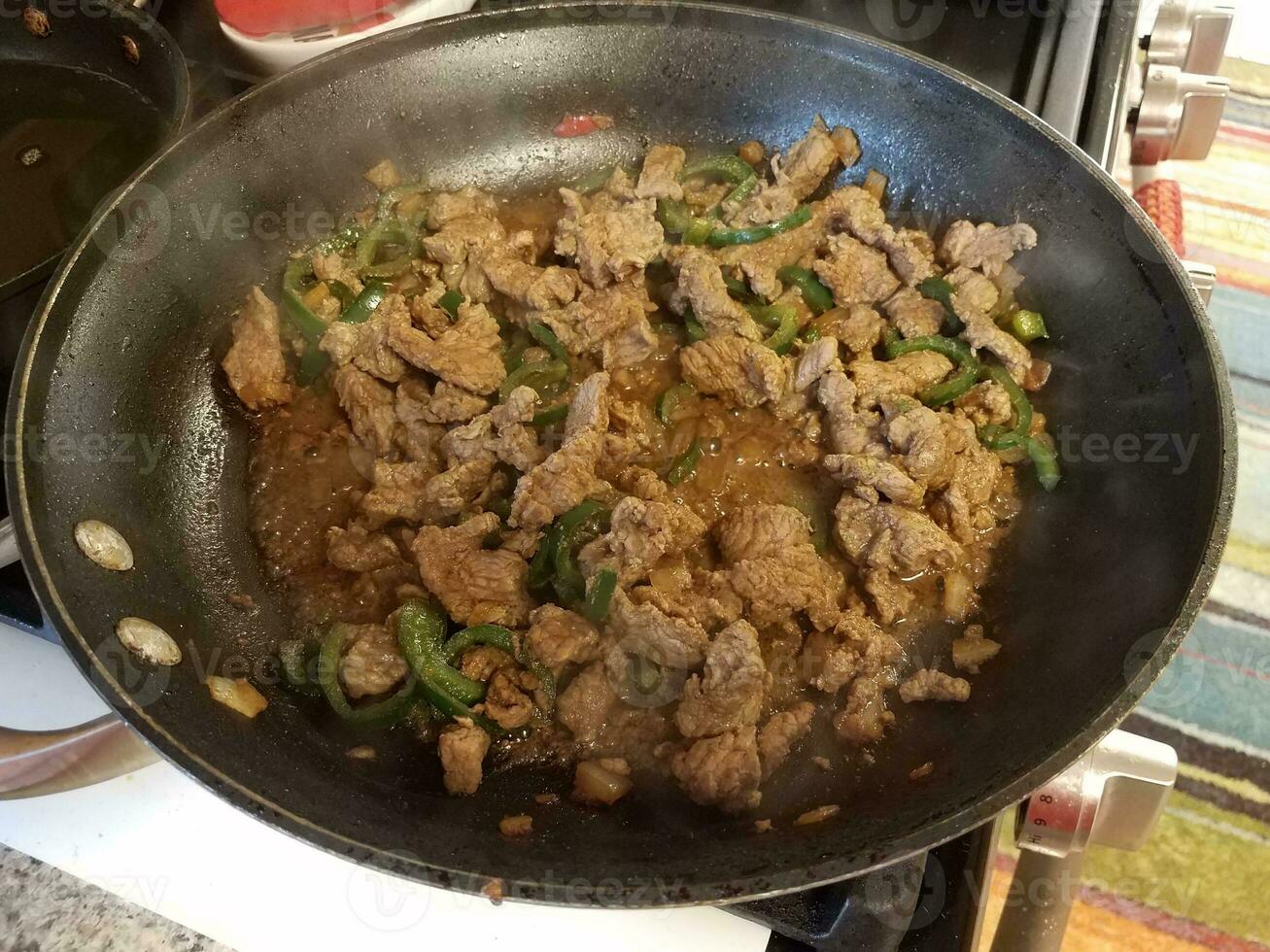 beef and green peppers in frying pan on stove photo