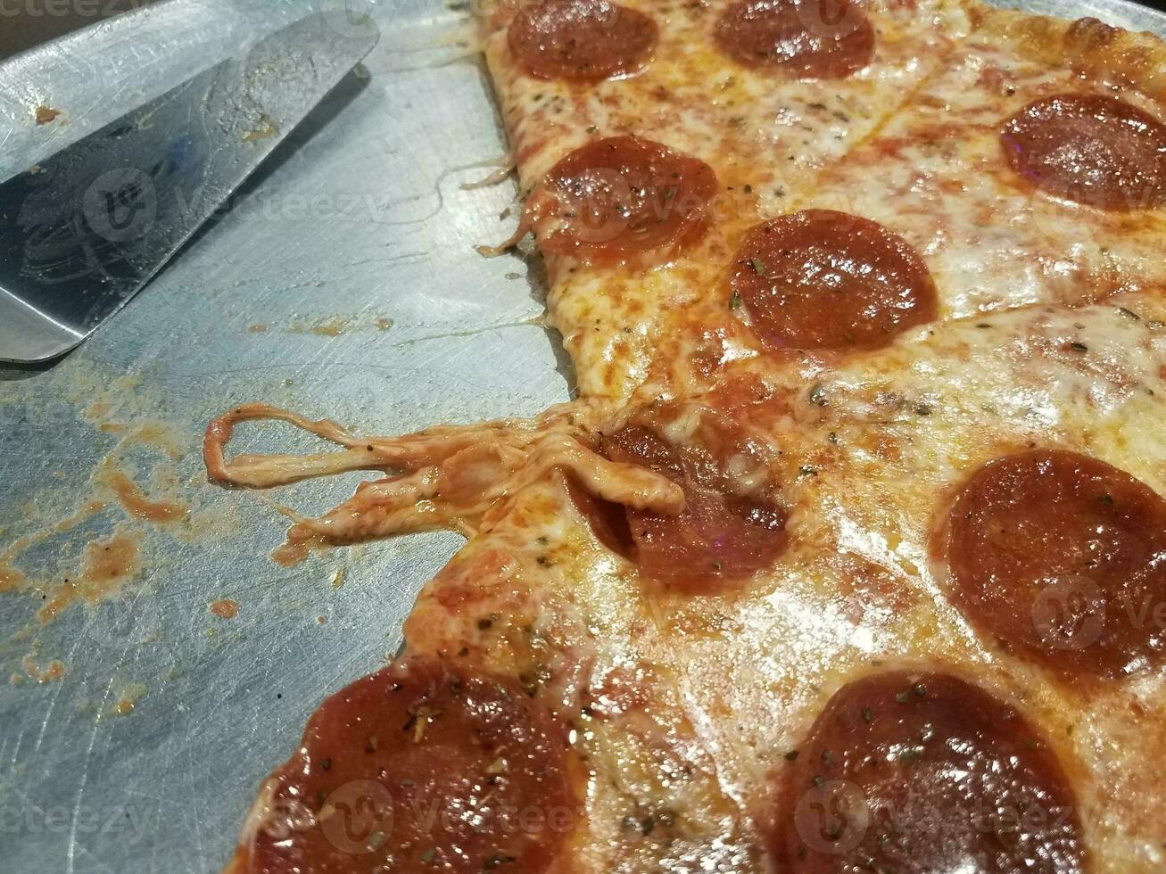 greasy cheese and pepperoni pizza on metal tray with spatula photo