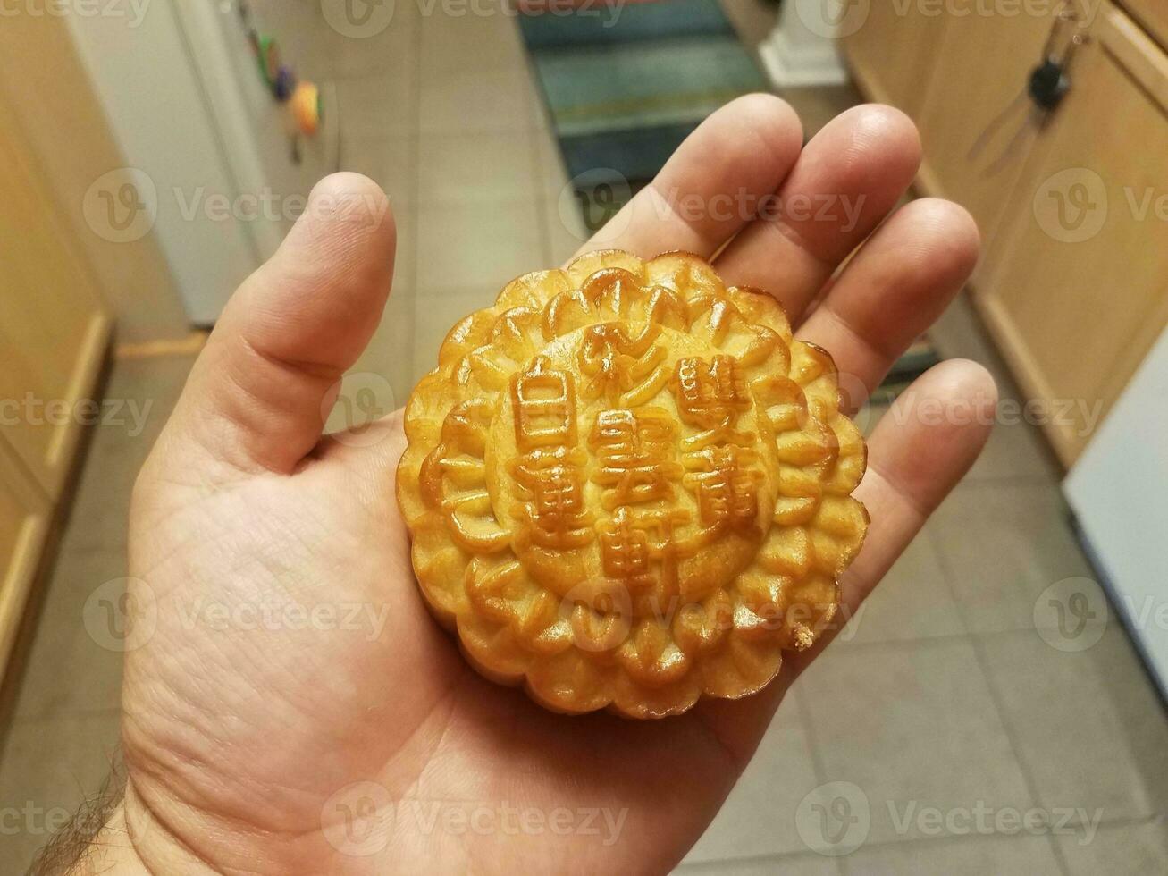 Mano sosteniendo pastel de luna chino en una cocina. foto