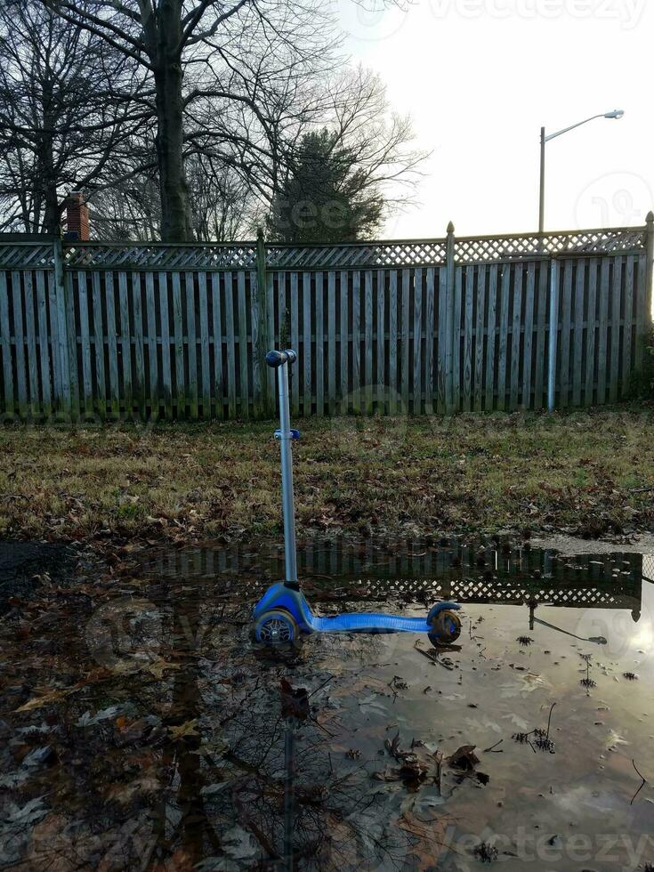 scooter azul en charco de agua y valla de madera foto