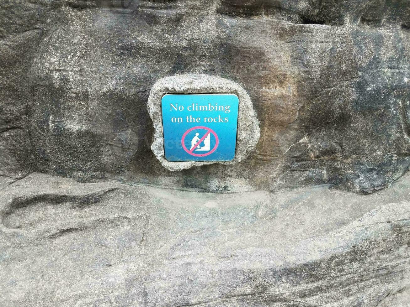 blue no climbing on the rocks sign with grey rock photo