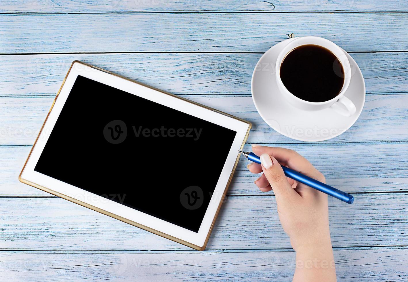 Tablet PC with black screen, near a cup of coffee on a wooden background, hand with a stylus, work process. Concept - Business, Online education photo