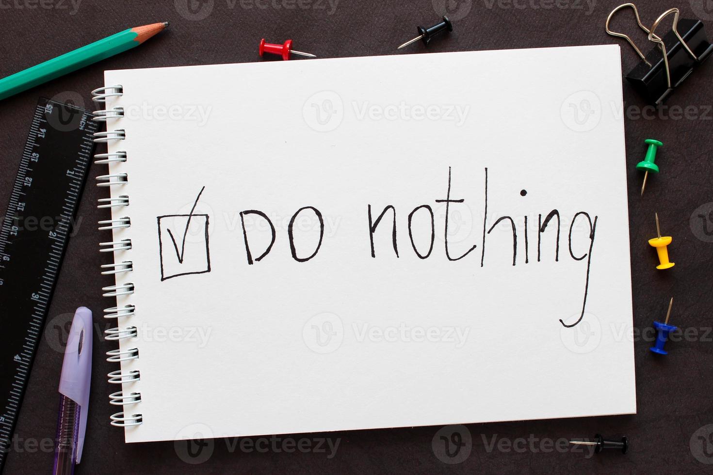 Words Do nothing with check mark on a notebook. Around the notebook are stationery. photo