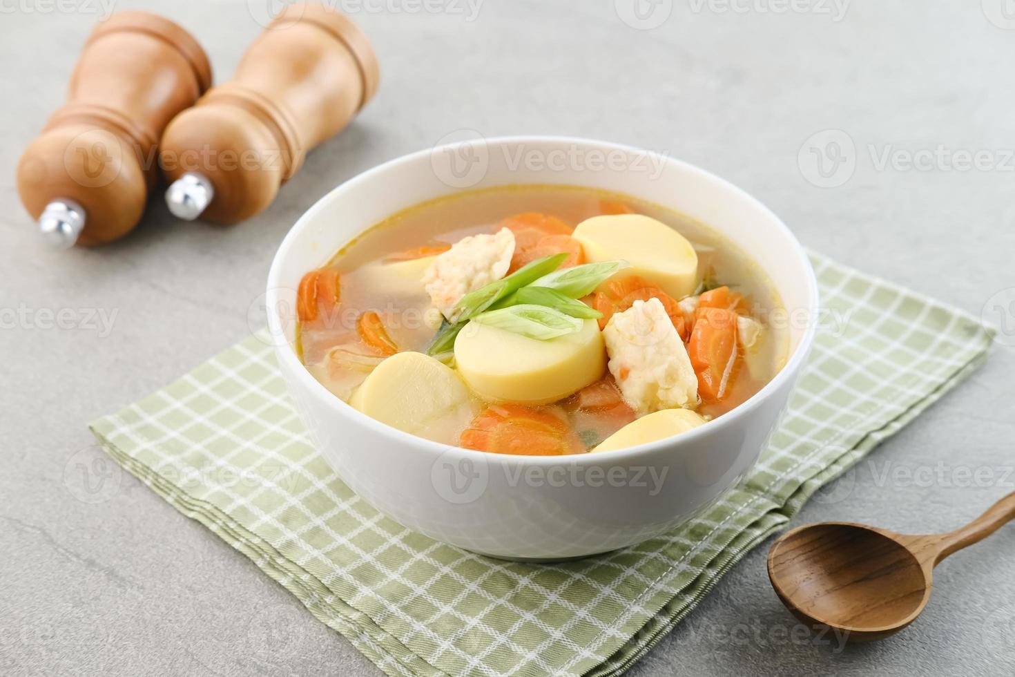 Sopa clara con tofu de huevo, albóndigas de zanahoria y gambas. servido en tazón blanco sobre fondo gris. foto