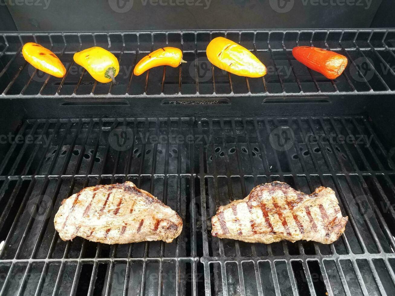 steaks on barbecue grill with colorful peppers photo