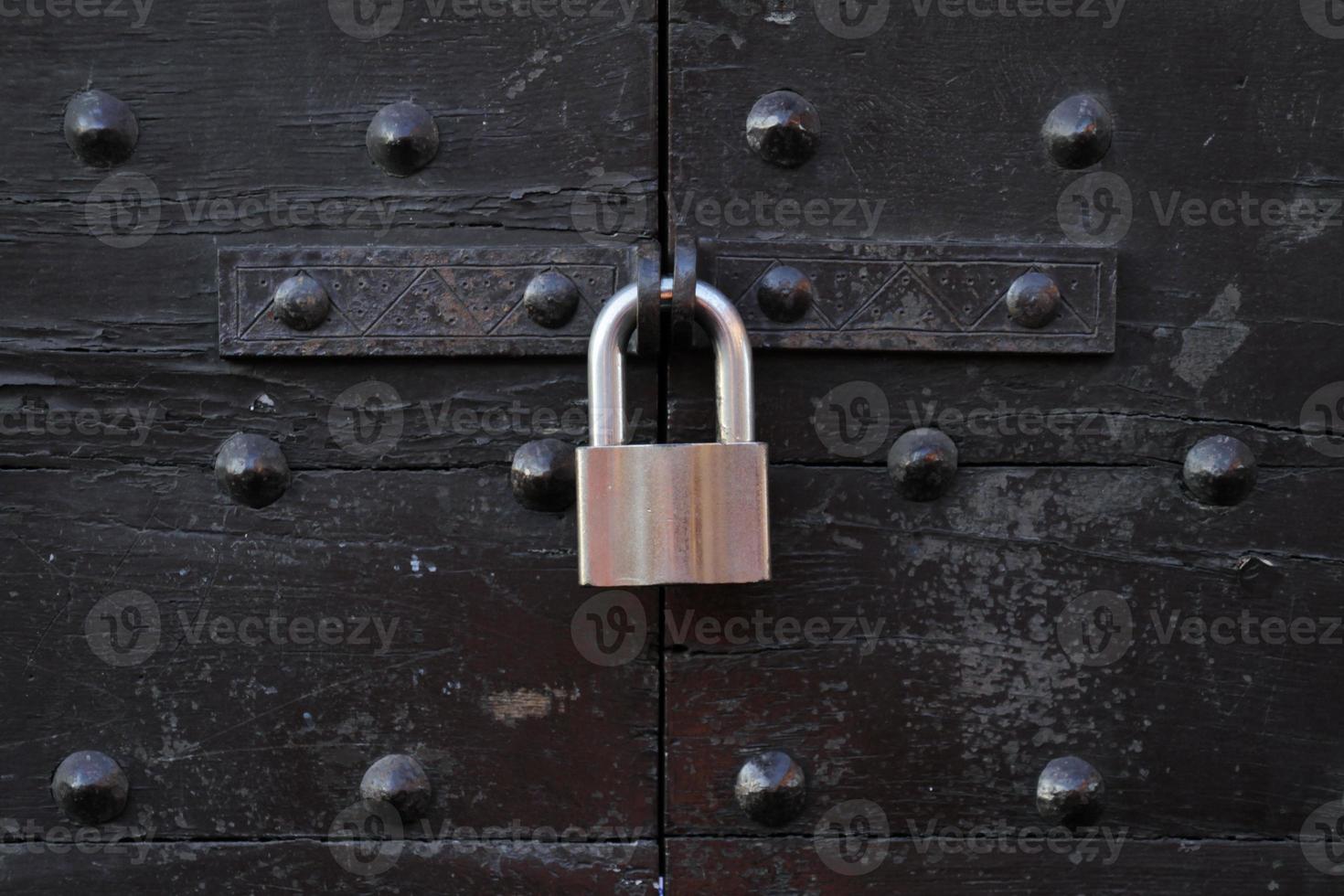 Metal padlock at an old wooden gate with metal bolts photo