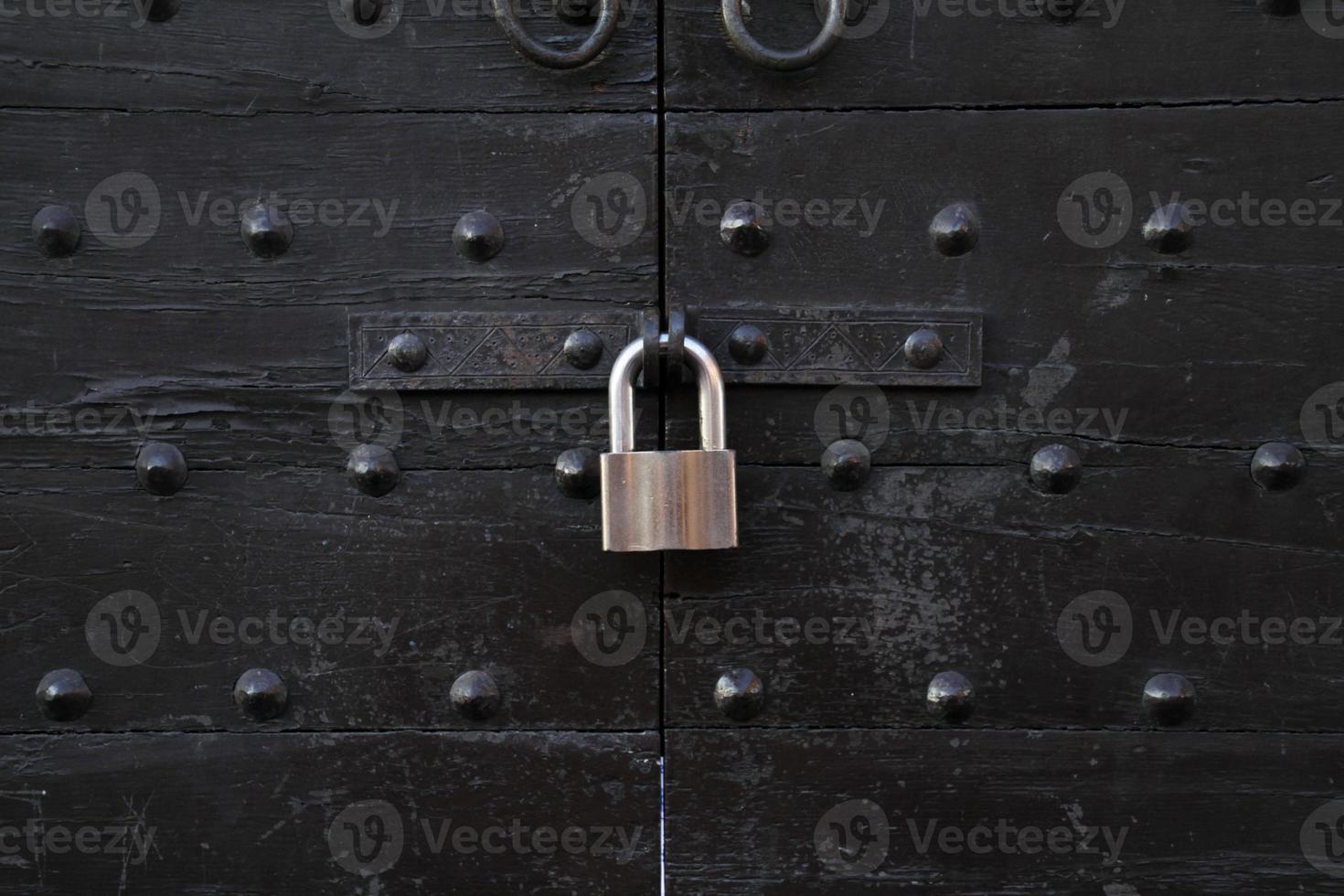 Metal padlock at an old wooden gate with metal bolts photo