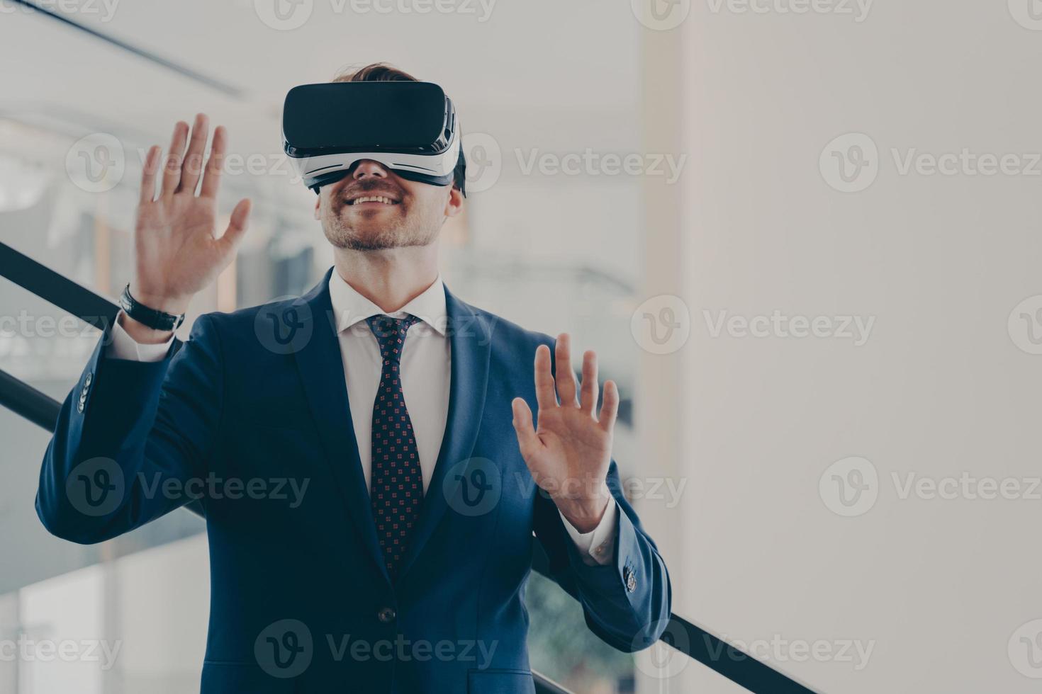 Businessman in virtual reality glasses standing on stairs in office and gesturing photo