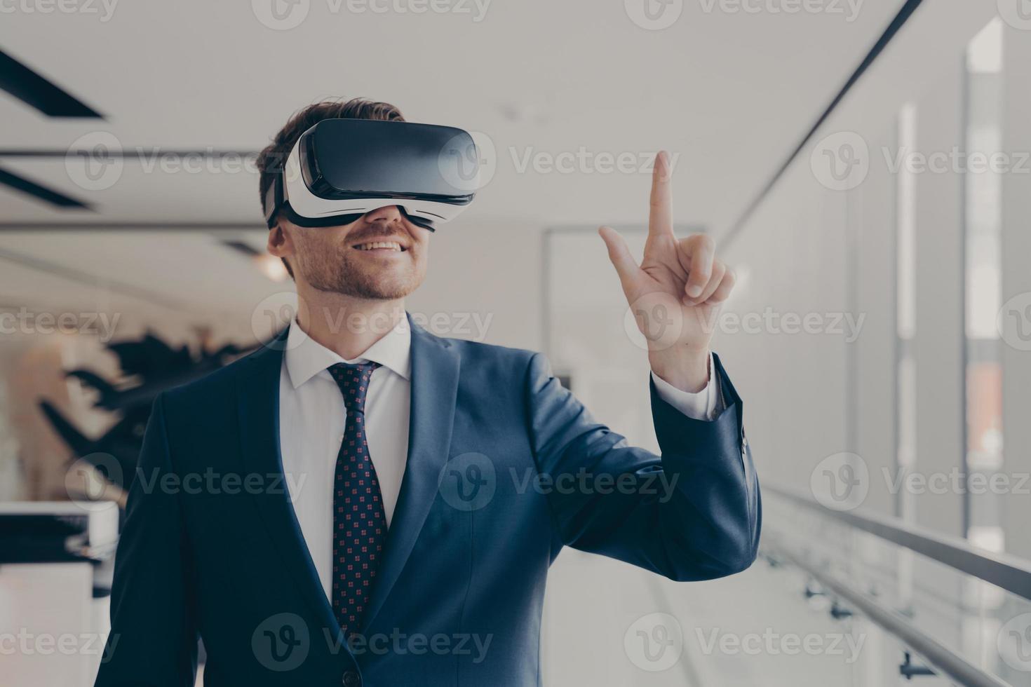 Cheerful businessman dressed formally using vr headset at work photo
