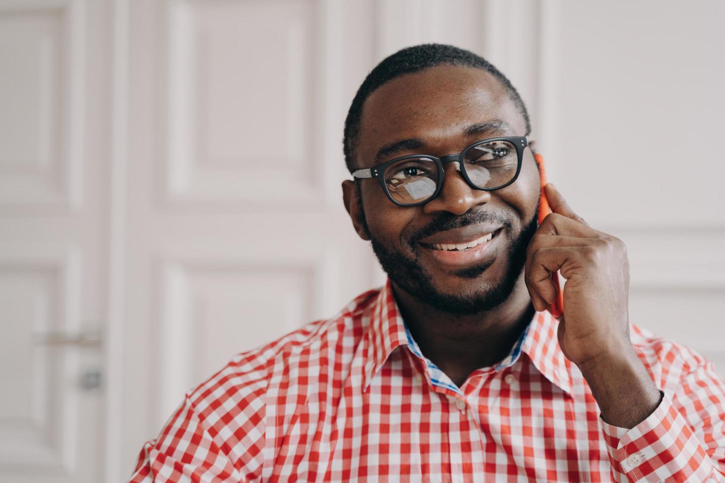 Smiling cheerful African man freelancer guy talking on mobile phone while working remotely photo