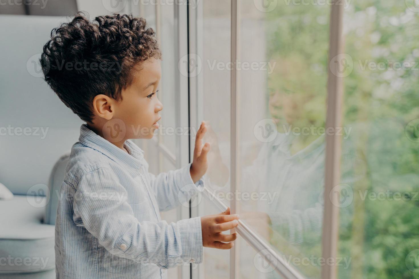 Sweet african american kid looking through window and waiting for parents photo