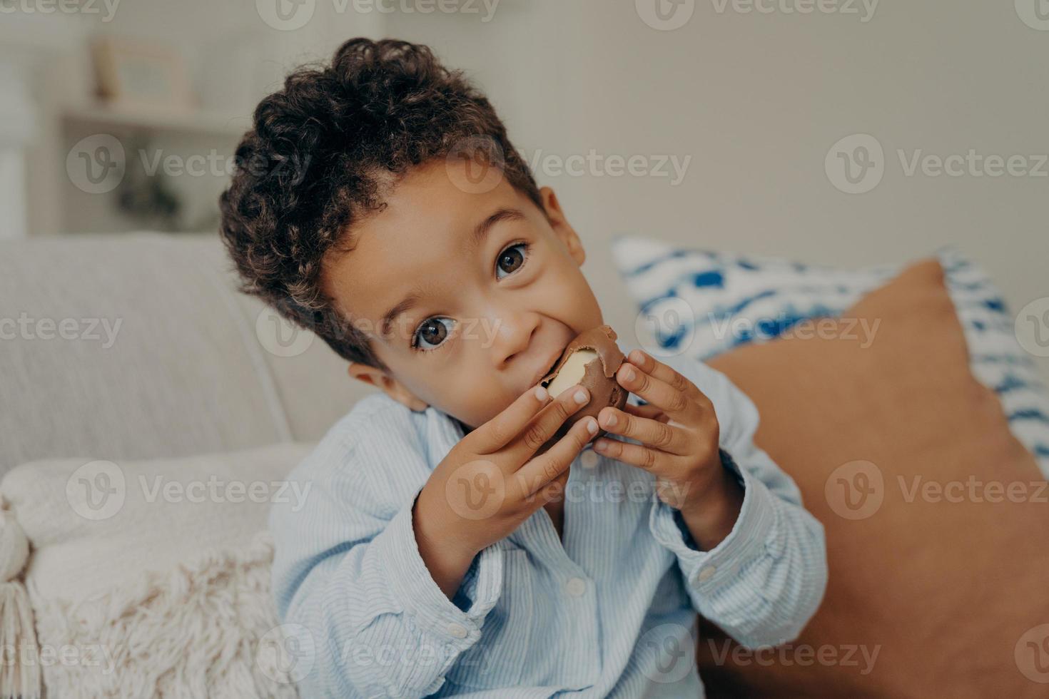 lindo niño mulato con grandes ojos color avellana comiendo dulces en casa foto