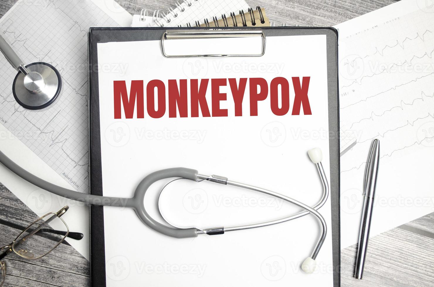 On a wooden background, a stethoscope, a pen and a paper folder with paper and the text MONKEYPOX. medical concept photo