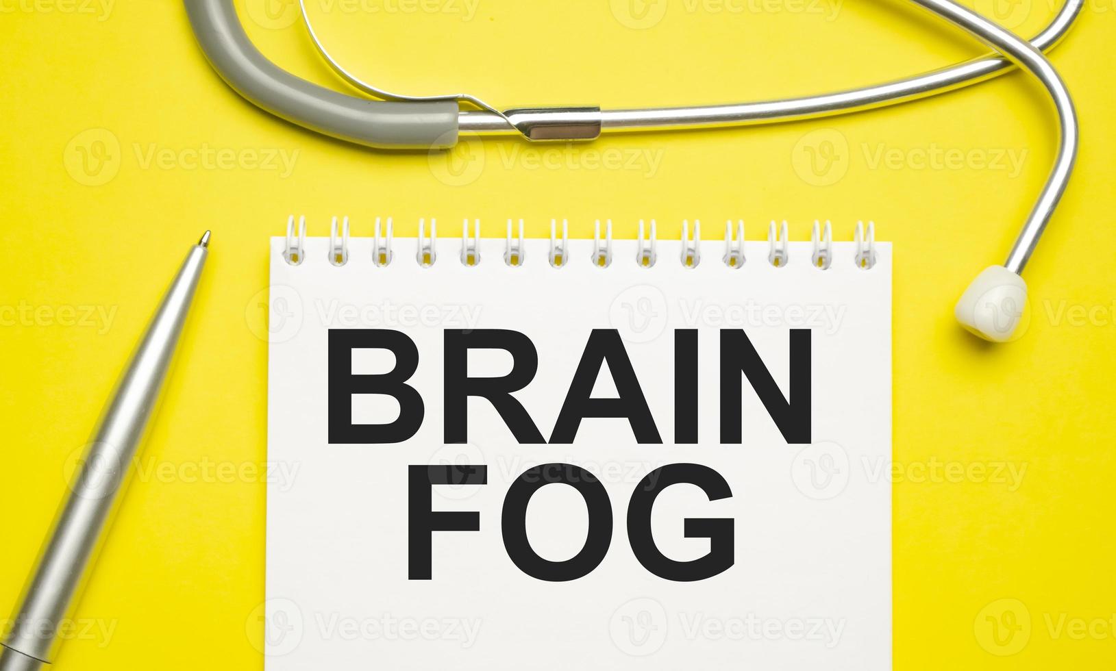 The word brain fog written on a white notepad on a yellow background photo