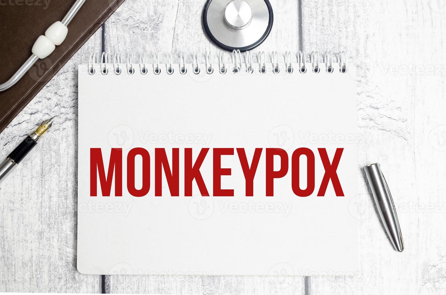 On a wooden background, a stethoscope, a pen and a paper folder with paper and the text MONKEYPOX. medical concept photo
