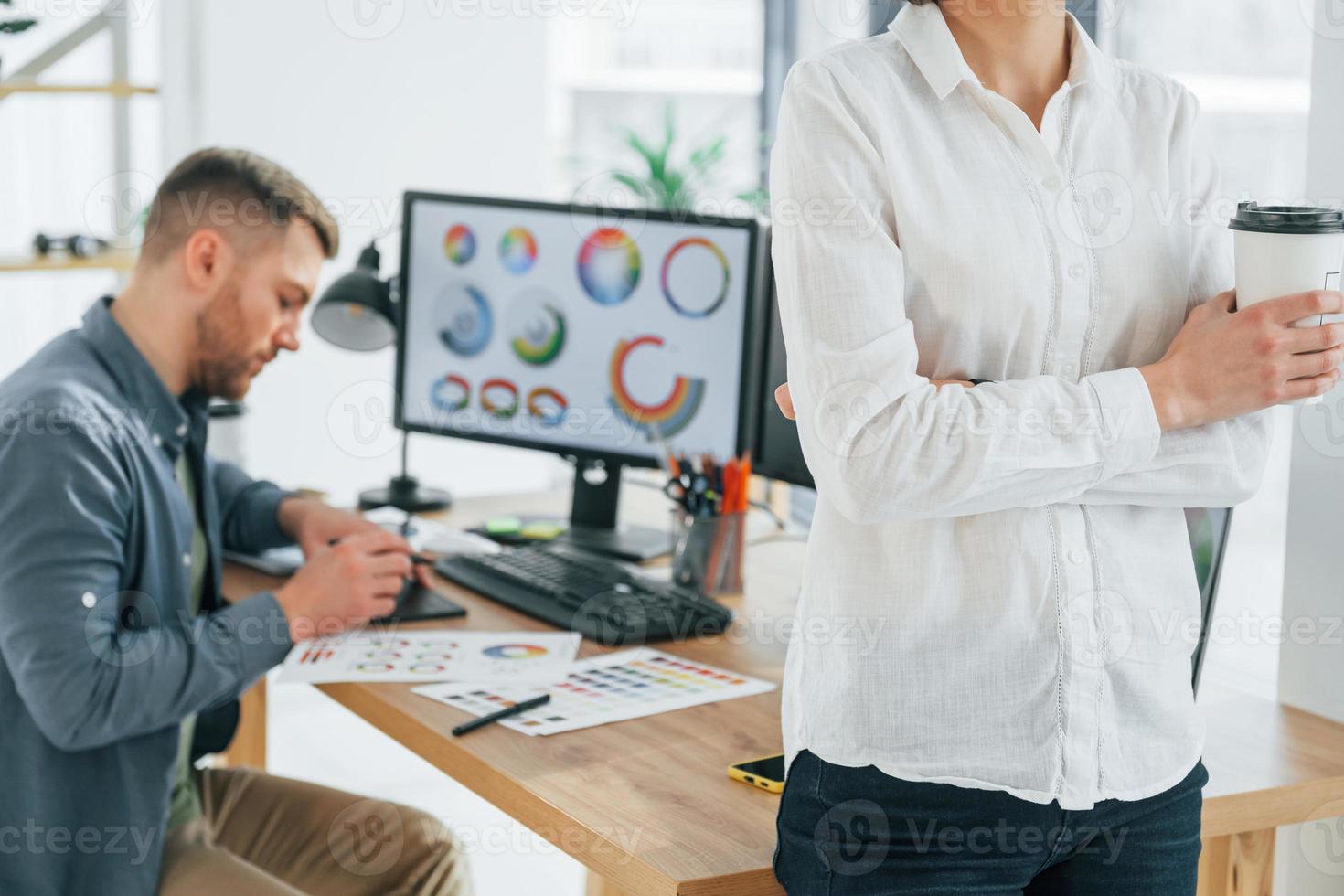 Woman standing in front of man that sitting by the table. Two designers working together in the office photo