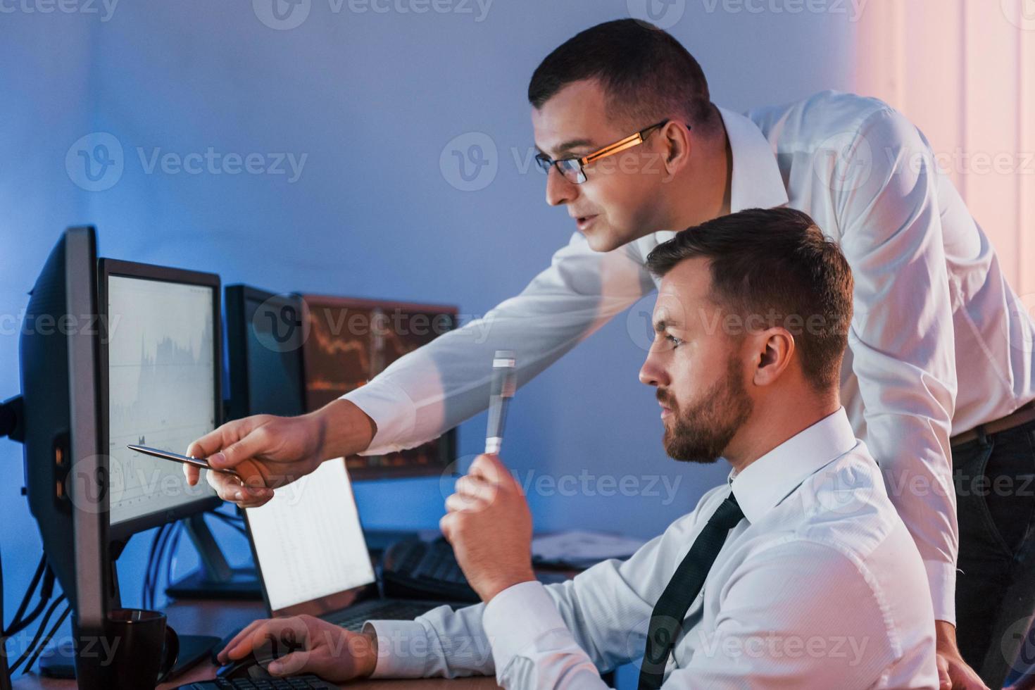 Many displays on the table. Two stock traders working in the office with exchange technology photo