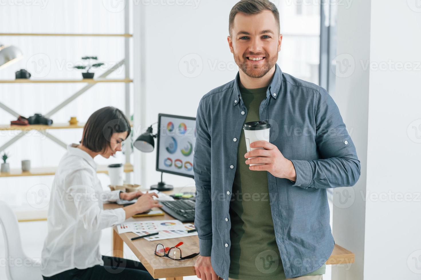 Positive man standing in front of woman that sitting by the table. Two designers working together in the office photo