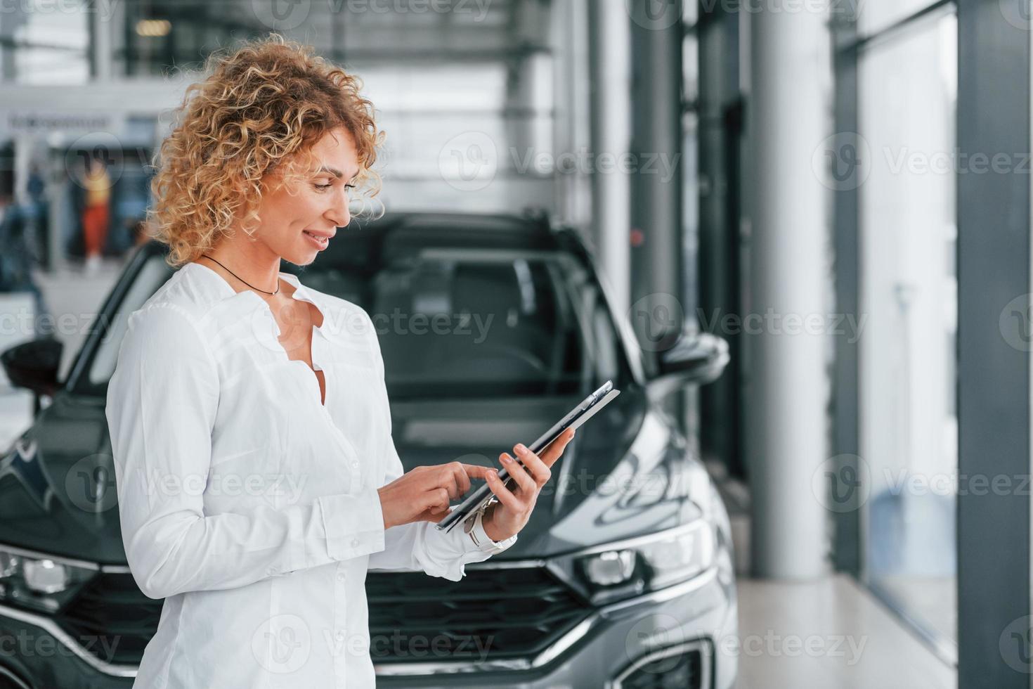 In official white shirt. Woman with curly blonde hair is in autosalon photo