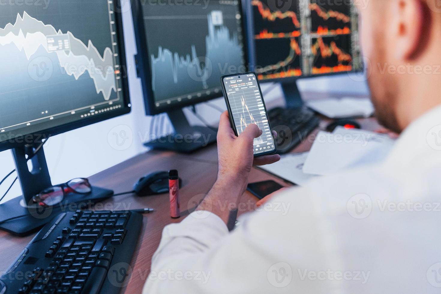 Using phone. Stock trader working in the office with exchange technology photo