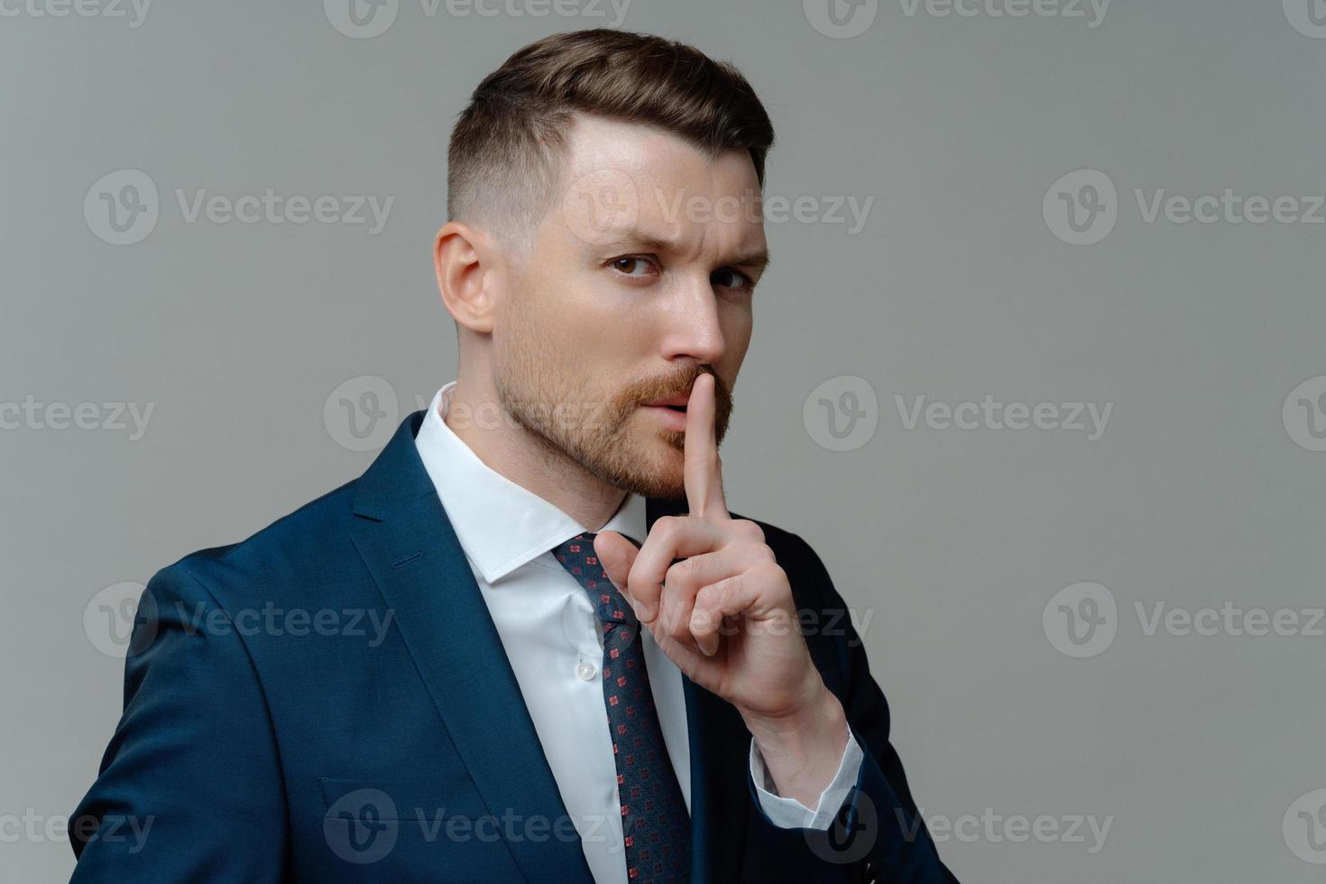 Serious businessman in suit showing silence sign photo