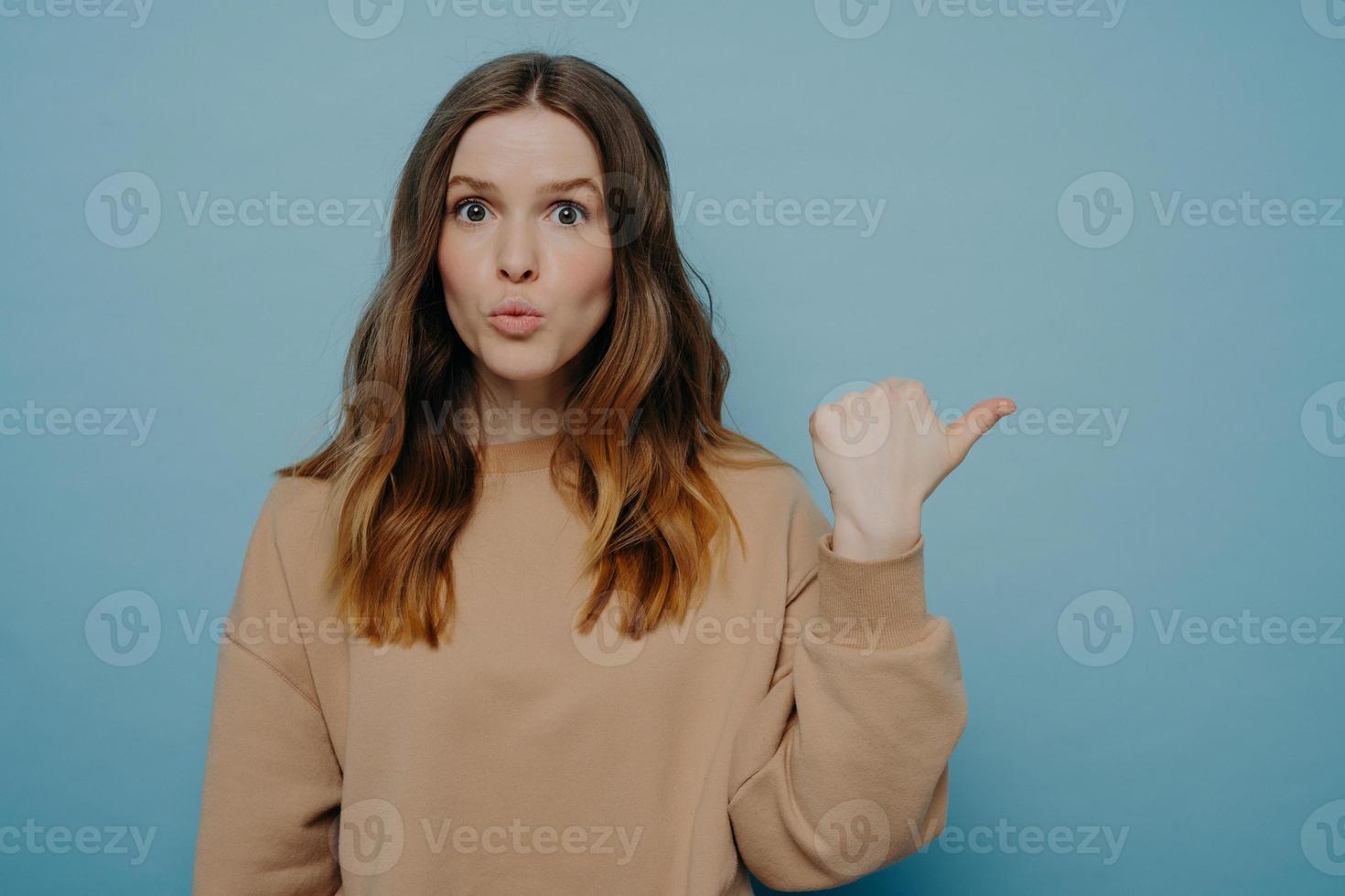 Surprised young woman pointing at copy space with wow expression photo