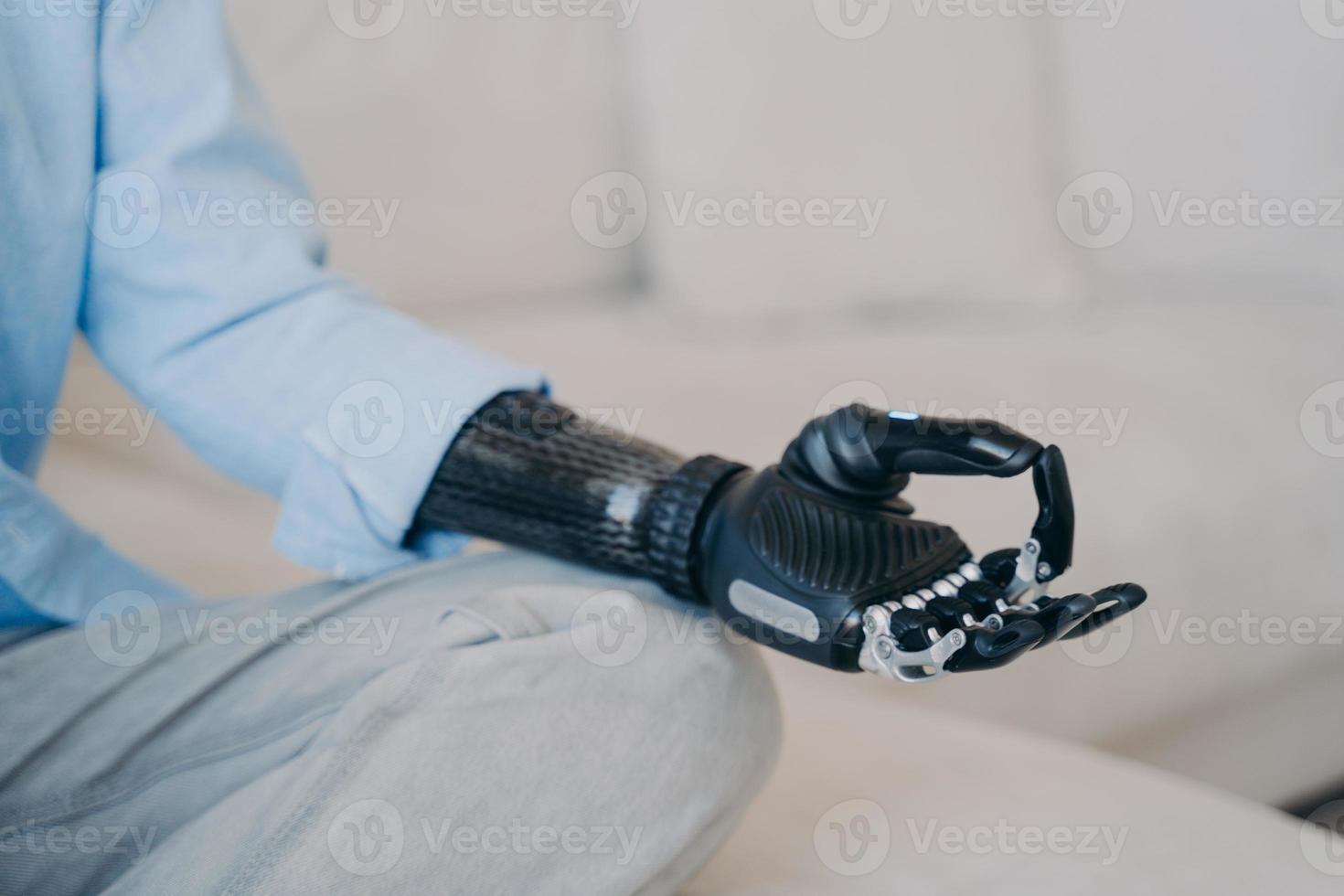 Cyber hand of disabled person which is sitting in lotus pose on couch. Robotic arm in meditation. photo