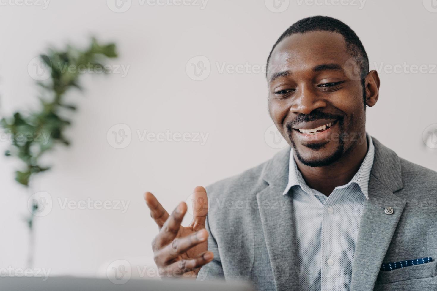 Smiling african american businessman holding a video call with customers on laptop, advises clients photo