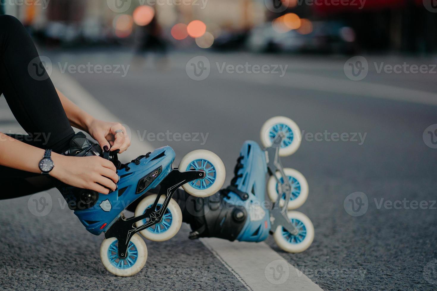 Legs of unrecognizable woman puts on rollerskates going to have exercises outdoor leads active lifestyle poses on street road prepares for inline skating. Faceless skater goes in for dangerous sport photo