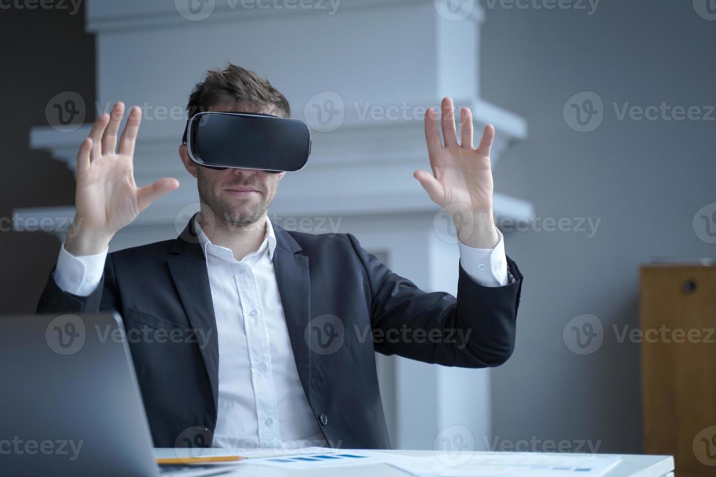 Man CEO in virtual reality glasses with hands up in air at home office interior photo