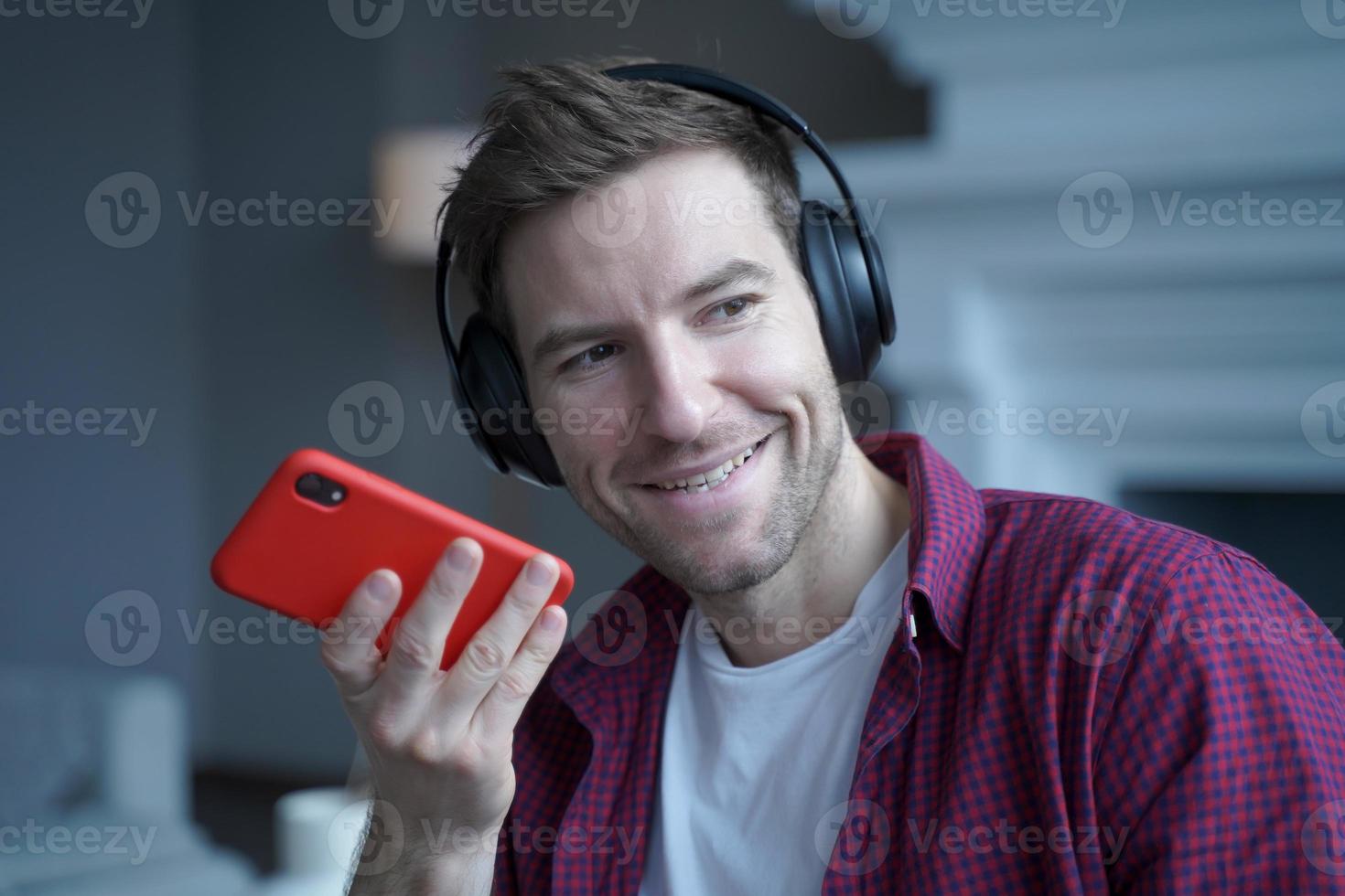 un joven alemán sonriente con auriculares grabando un mensaje de voz para un colega, usando un altavoz foto