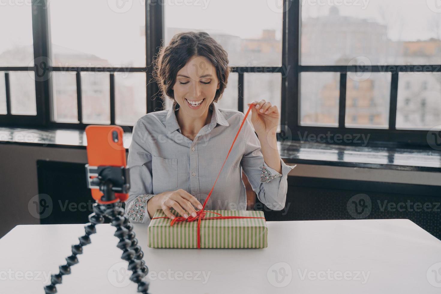 Excited hispanic woman blogger opening gift box recording video about xmas present for her blog photo