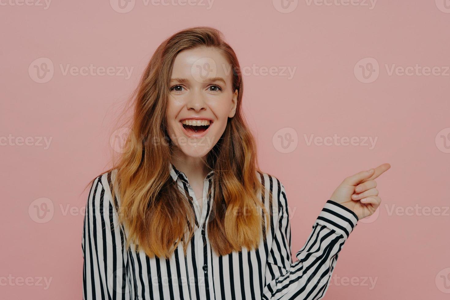 Laughing young female pointing aside at copy space for advertisement with forefinger photo