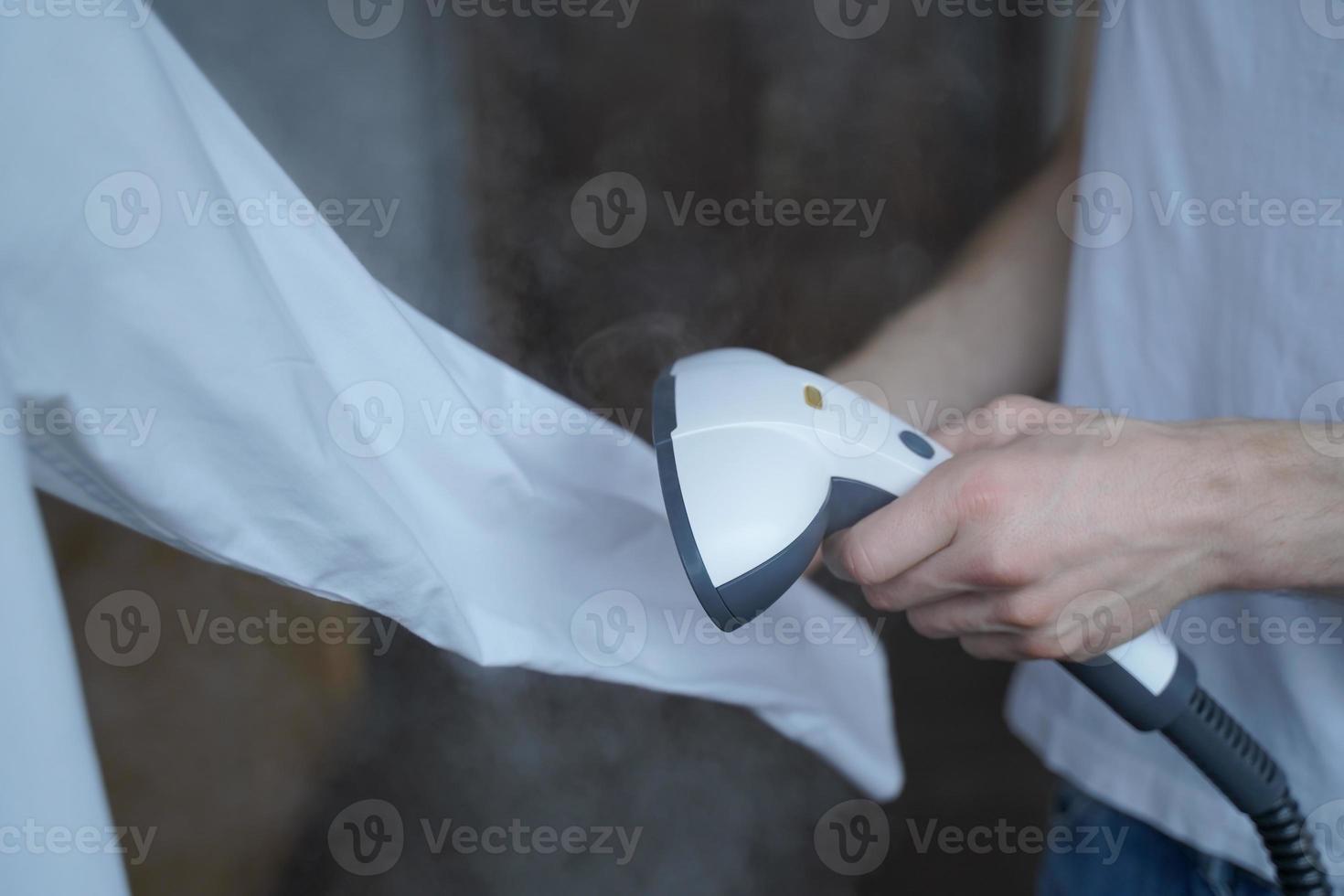 Cropped photo of man using steamer neatly ironing white shirt while holding long sleeve