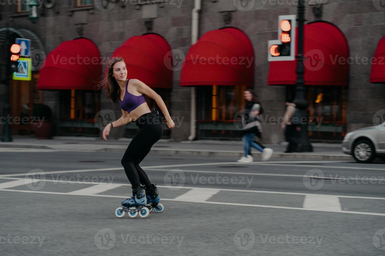 Slim sporty young woman uses rollerskates as mode of transportation in city enjoys favorite hobby ans boosts mood dressed in active wear poses on road exercises regularly keeps fit loses weight photo