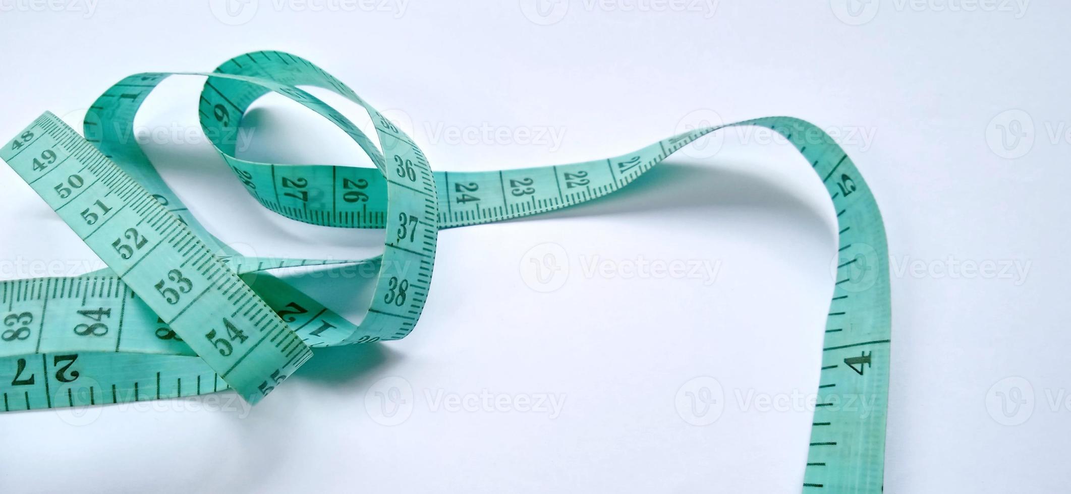 Old wrinkled green rubber tape measure with negative space. Rubber tape measure isolated on the gray white background. Useful for sewing cloth or fabric. photo