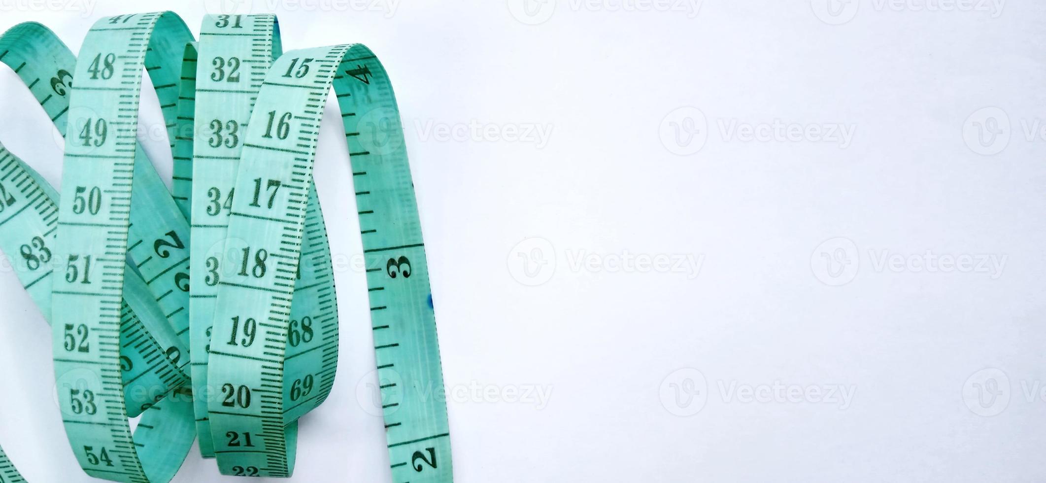 Old wrinkled green rubber tape measure with negative space. Rubber tape measure isolated on the gray white background. Useful for sewing cloth or fabric. photo