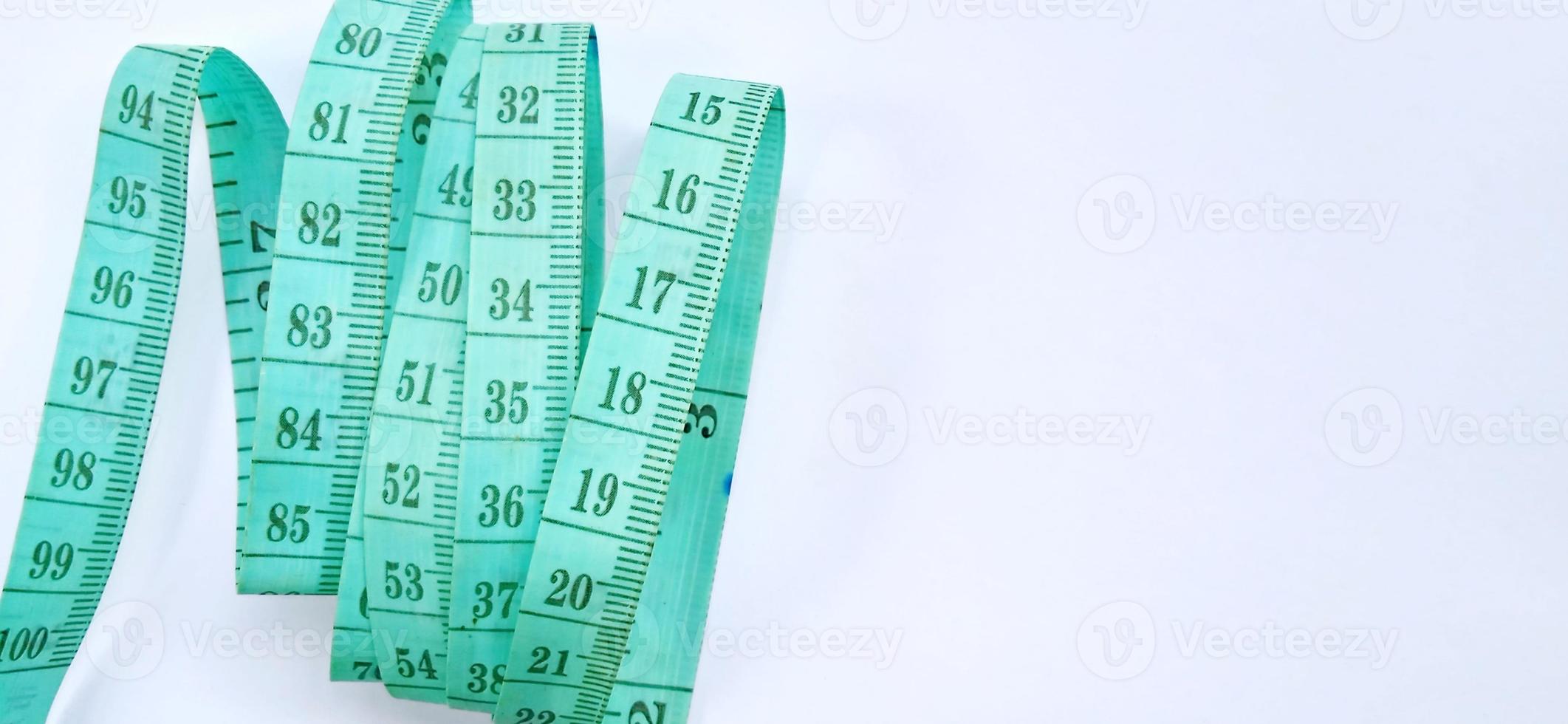 Old wrinkled green rubber tape measure with negative space. Rubber tape measure isolated on the gray white background. Useful for sewing cloth or fabric. photo