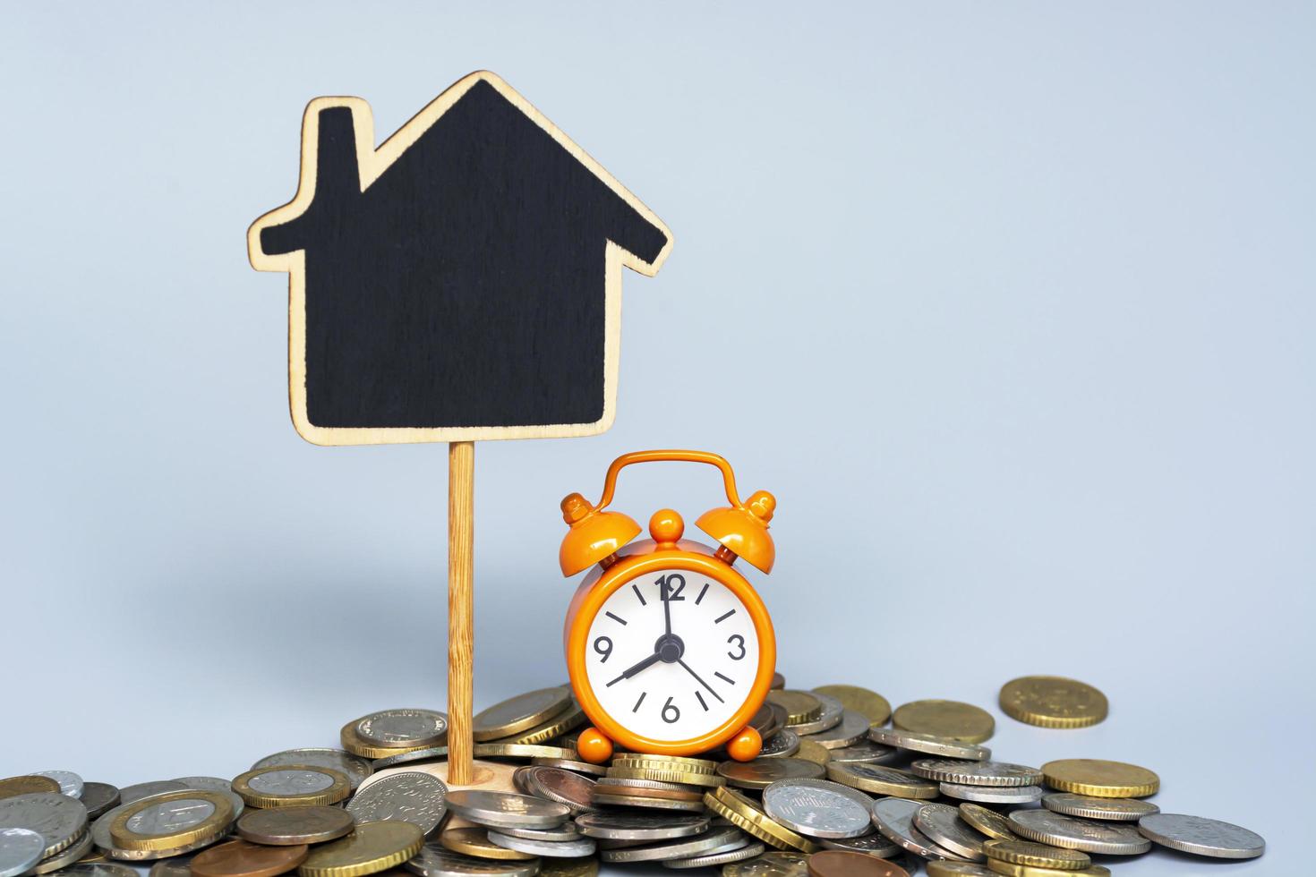 Wooden house model and alarm clock set at eight o'clock with pile of coins on blue background. Business, finance, savings, money management, property loan or mortgage concept. photo