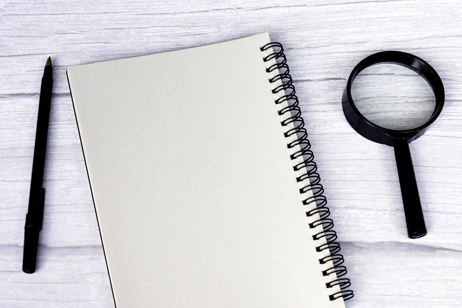 Blank notepad with pen, and magnifying glass on a white wooden table. Flat lay. photo