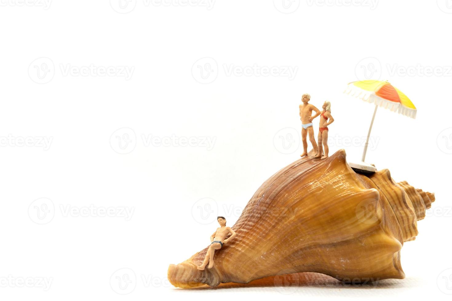 Miniature people wearing swimsuit relaxing on seashells with white background photo