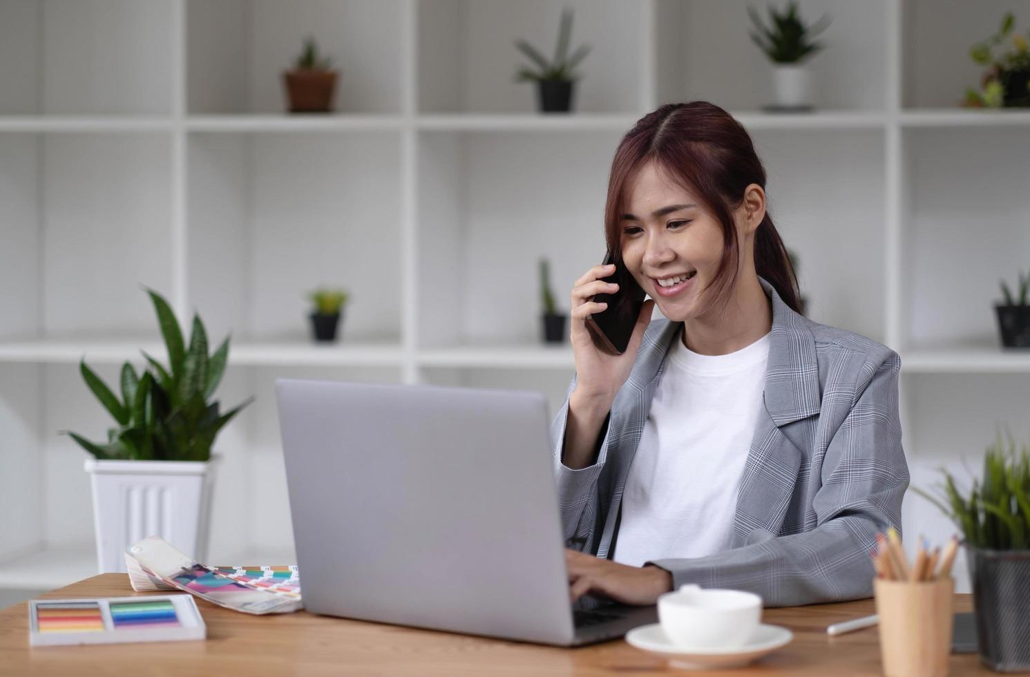 Asian woman designer working using a smartphone blank white computer screen placed at table with color samples photo