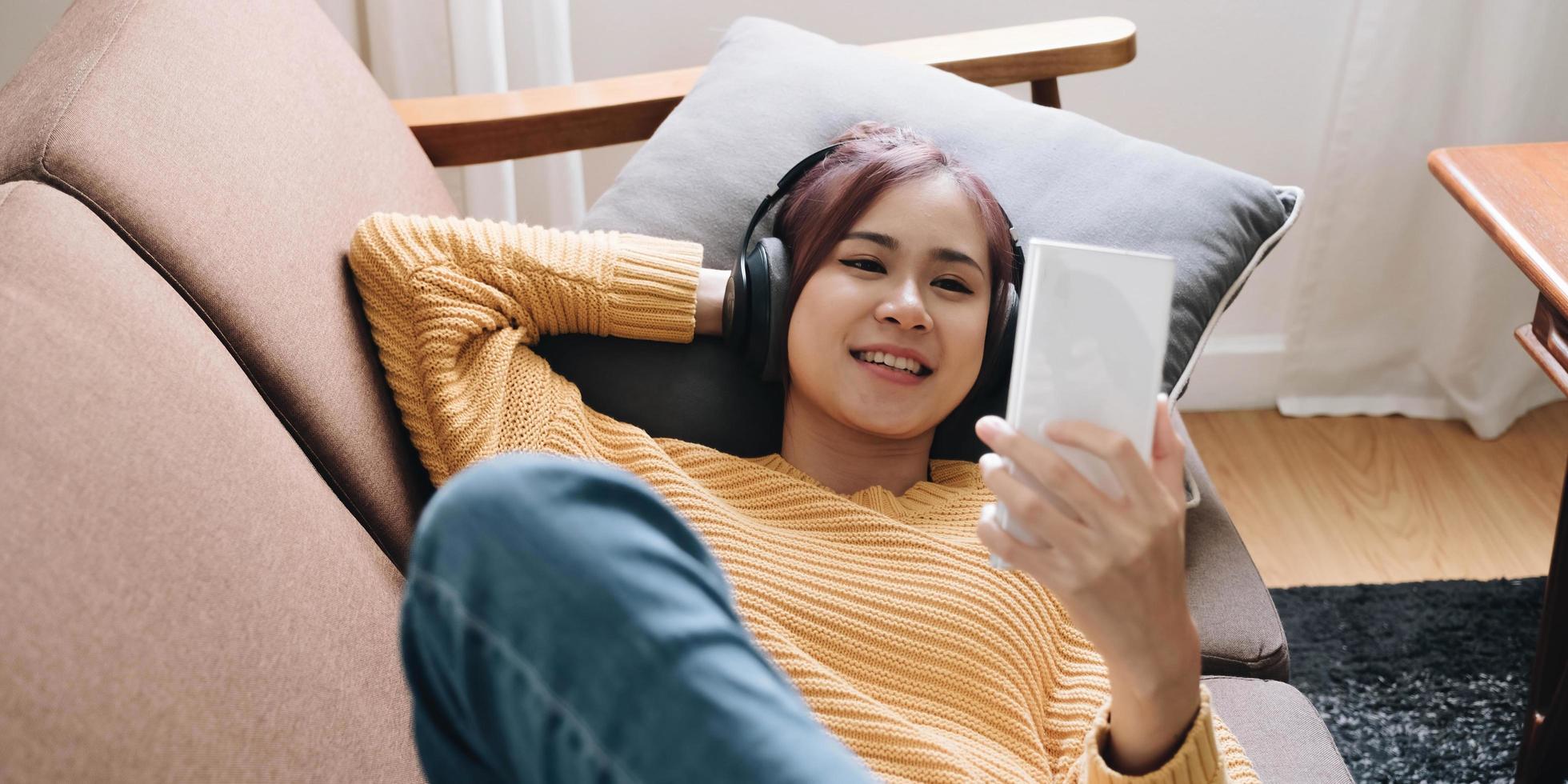 Close up smiling attractive woman in headphones using smartphone, lying on couch, positive young female looking at phone screen, watching video or making call, chatting online, listening music photo
