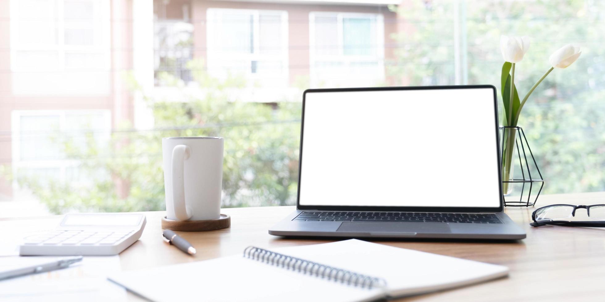 Modern office desk with open laptop computer white screen mockup, financial and marketing report, calculator and supplies. photo