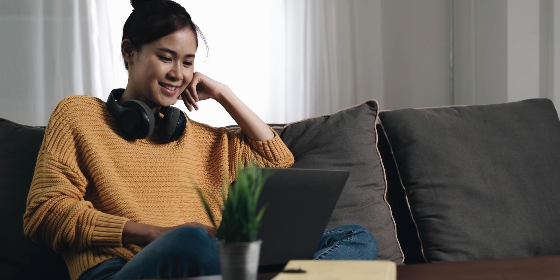 Cheerful freelancer working on laptop sitting on couch and listening to music in headphones, copyspace photo