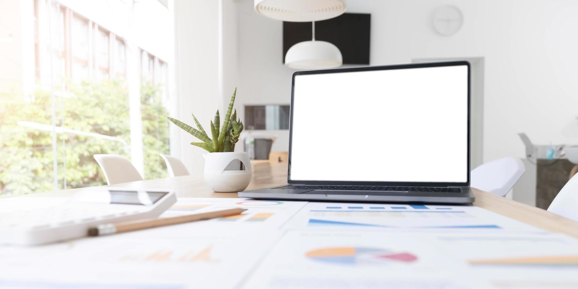 escritorio de oficina moderno con maqueta de pantalla blanca de computadora portátil abierta, informe financiero y de marketing, calculadora y suministros. foto